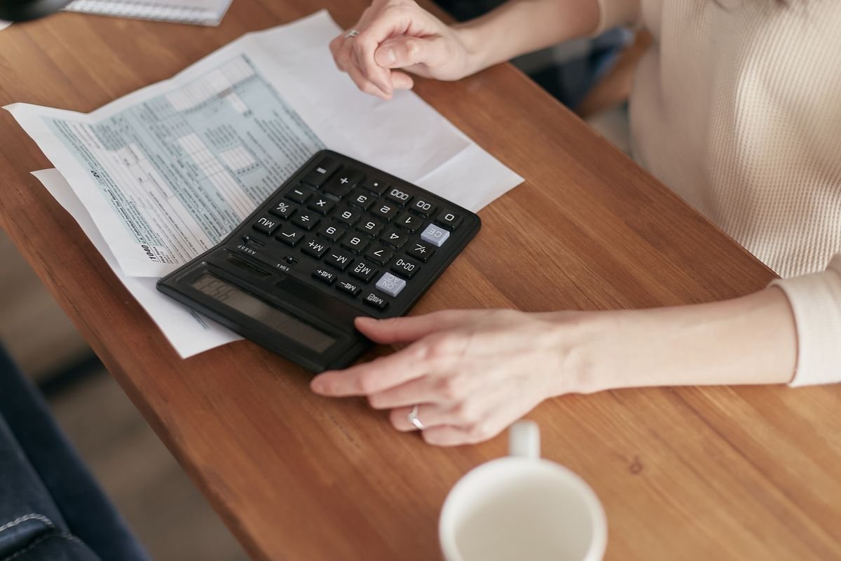 Person using a calculator on a wooden desk to work out a monthly budget.